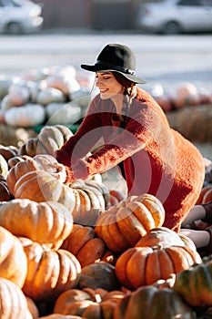 Portrait of happy woman choosing ripe orange pumpkin on farmers market in brown sweater, dress. Cozy autumn vibes Halloween,