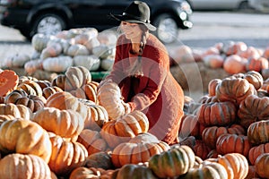 Portrait of happy woman choosing ripe orange pumpkin on farmers market in brown sweater, dress. Cozy autumn vibes Halloween,