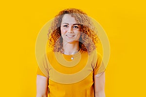 Portrait of a happy woman with curly red hair over yellow background