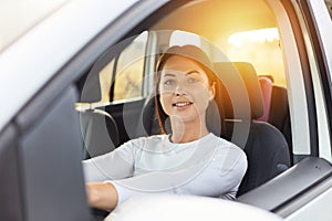 Portrait of happy woman driving a car and smiling, cute young success brunette woman driver steering car, wearing white shirt,