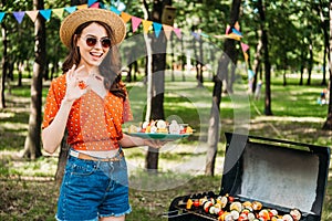 portrait of happy woman in hat and sunglasses with grilled vegetables on plate showing ok sign