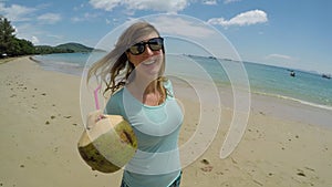 PORTRAIT: Happy woman having fun at the beach while holding a coconut drink.