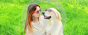 Portrait of happy woman with her Golden Retriever dog wearing sunglasses on green grass in summer park