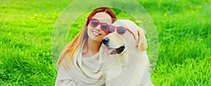 Portrait of happy woman with her Golden Retriever dog wearing sunglasses on green grass in summer park