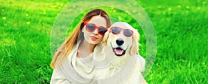 Portrait of happy woman with her Golden Retriever dog wearing sunglasses on green grass in summer park