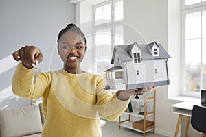 Portrait of a happy woman holding a house model and showing the key to her new home