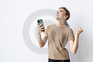 Portrait of a happy woman holding mobile phone and celebrating a win isolated over white background