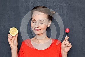 Portrait of happy woman holding sour lemon and sweet lollipop