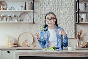 Portrait of happy woman at home, asian woman eating healthy food salad and smiling, housewife looking at camera sitting