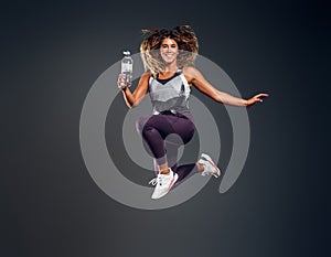 Portrait of happy woman jumping with bottle of water