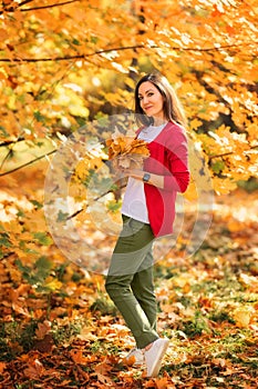 Portrait of happy woman with long hair playing with yellow autumn leaves in park during fall outdoor.