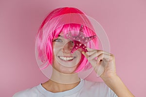 portrait of a happy woman with pink hair holding red star fish near her face and smiling against pastel  pink background