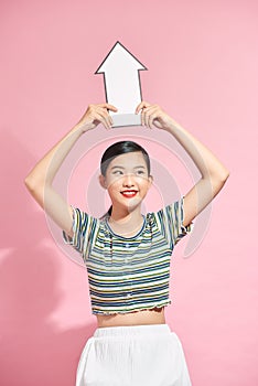 Portrait of a happy woman pointing away with an arrow while standing isolated over pink background