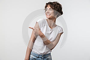 Portrait of happy woman with short hair in basic t-shirt rejoicing and pointing finger at copyspace