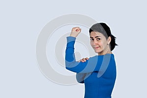 Portrait of a happy woman showing her biceps on gray background. Strong, determined, confident woman pointing to her biceps