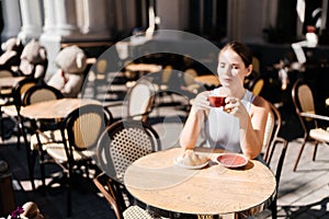 Portrait of happy woman sitting in a cafe outdoor drinking coffee. Woman while relaxing in cafe at table on street