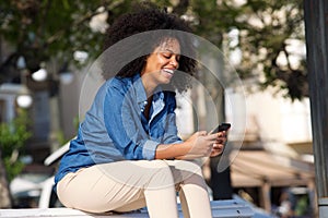 Happy woman sitting outside with mobile phone photo