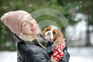 Portrait of happy woman and spaniel dog in winter forest. Woman hold in hands cute little spaniel. Walking in snowfall.