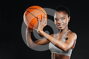 Portrait of happy woman in sportswear holding basketball over black