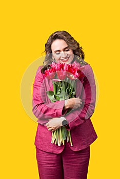 Portrait of happy woman in suit embracing bunch of pink tulips