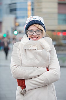 Portrait of happy woman in warm clothing standing arms crossed on city street