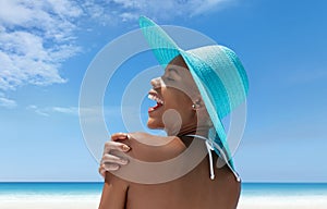 Portrait of happy woman wearing sun hat in hot summer beach, enjoying a holiday by the sea. Seen from behind, with her hand on her