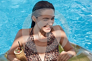 Portrait of happy woman with wet dark hair, having rest in swimming pool, having fun and drinking cocktail. Beautiful glamour girl