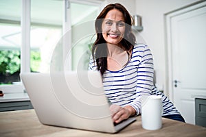 Portrait of happy woman working on laptop while holding coffee mug