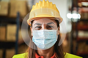 Portrait of happy worker woman looking at camera inside warehouse while using face mass - Focus on face