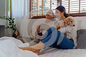 Portrait of happy young adult Asian couple on bed along with dog pet in bedroom interior scene. Man and woman are