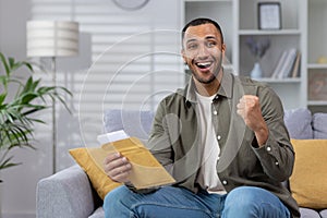 Portrait of happy young African American male student receiving good news from university. Holds a letter, message