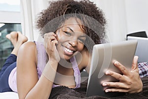 Portrait of happy young African American woman using tablet PC in bed