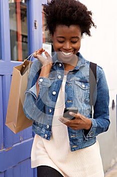 Happy young african american woman walking with cellphone and shopping bags