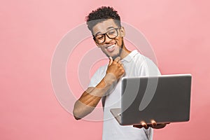 Portrait of happy young afroamerican man using laptop comruter and checkin isolated against pink