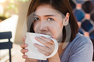 Portrait of happy young asian business woman with mug in hands drinking coffee in the morning at cafe.