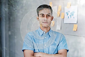 Portrait of Happy Young Asian Businessman standing by the Window Crossed Arms and Smiling in Office