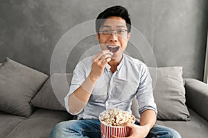 Portrait of a happy young asian man eating popcorn