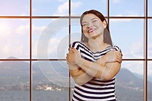 Portrait of happy young asian woman hugging herself.