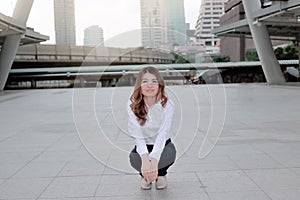 Portrait of happy young Asian woman posing in a squatting position on sidewalk at urban city background.