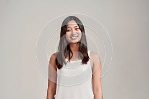 Portrait of happy young asian woman wearing white shirt smiling at camera while standing isolated over grey background