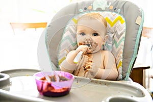 A Portrait Of Happy Young Baby girl In High Chair eat chocolate