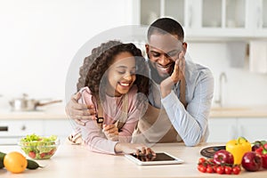 Black man and girl cooking in kitchen using digital tablet