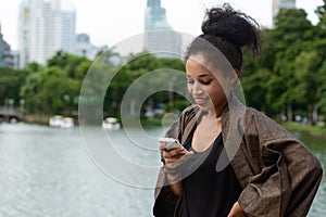 Portrait of happy young beautiful African woman using phone at the park