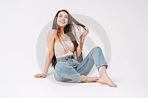 Portrait of happy young beautiful asian woman with dark long hair in jeans sitting on white background isolated