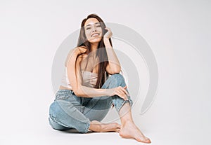 Portrait of happy young beautiful asian woman with dark long hair in jeans sitting on white background isolated