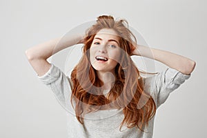 Portrait of happy young beautiful redhead girl smiling looking at camera touching hair over white background.