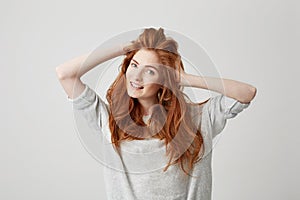 Portrait of happy young beautiful redhead girl smiling looking at camera touching hair over white background.