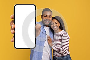 Portrait of happy young black couple presenting cellphone with mockup