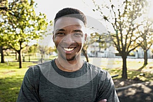 Portrait of happy young black man in sports clothing looking at camera and smiling in park