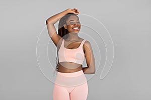 Portrait of happy young black woman in sports outfit posing and smiling on grey studio background